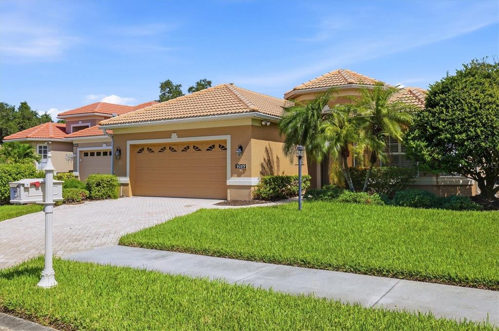 A tan single-story house with a tiled roof, a two-car garage, and a manicured lawn — 9089 WILLOW BROOK DRIVE, SARASOTA, FL