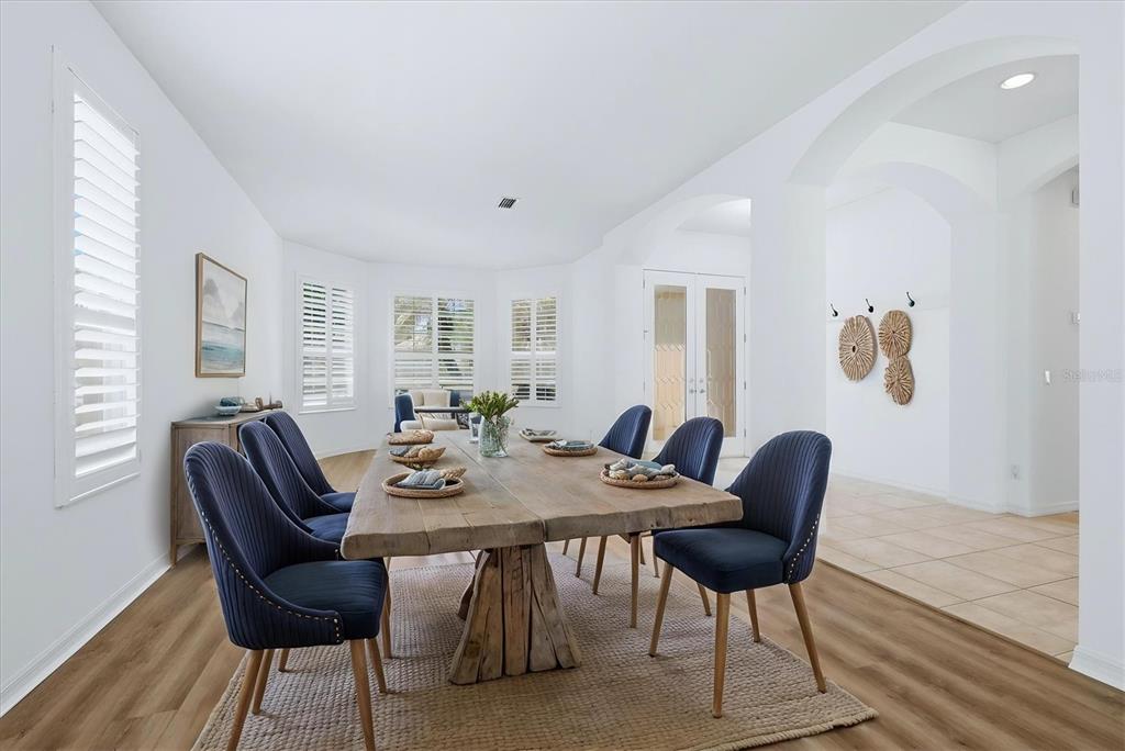 A dining room features a rustic wooden table, blue upholstered chairs, and white walls — 9089 WILLOW BROOK DRIVE, SARASOTA, FL