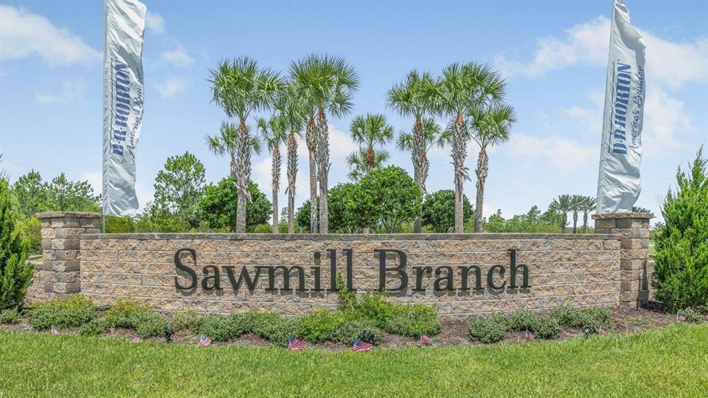 A stone monument sign for Sawmill Branch stands in a grassy area with palm trees — 164 SPRINGWOOD DRIVE, PALM COAST, FL