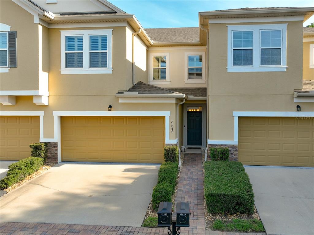 A two-story townhouse exterior features tan stucco walls, two garage doors, and a paved walkway — 17457 CHATEAU PINE WAY, CLERMONT, FL