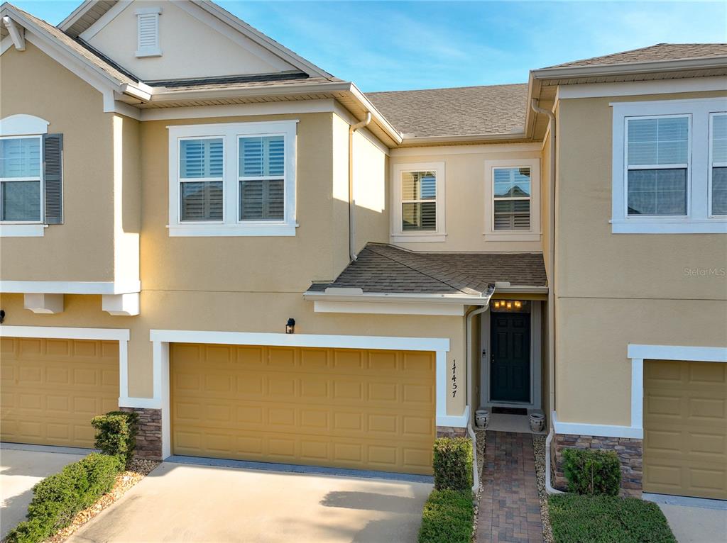 An exterior view of a two-story tan townhouse with a two-car garage and brick walkway — 17457 CHATEAU PINE WAY, CLERMONT, FL
