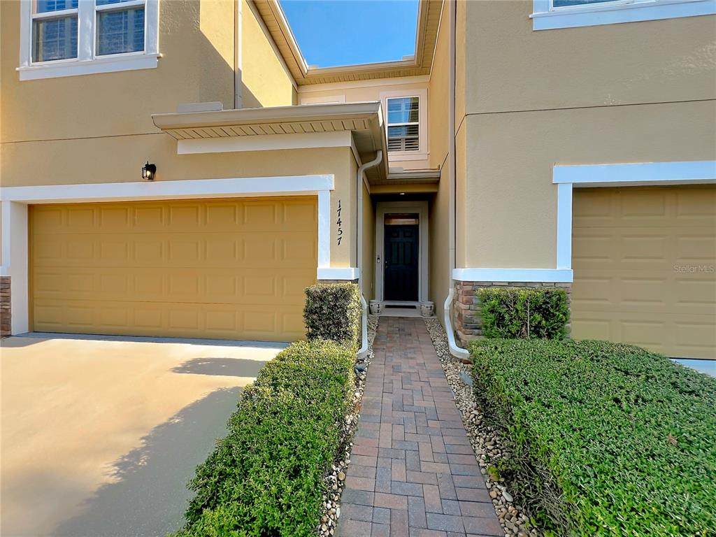 A two-story house exterior features a paved walkway leading to a dark front door — 17457 CHATEAU PINE WAY, CLERMONT, FL