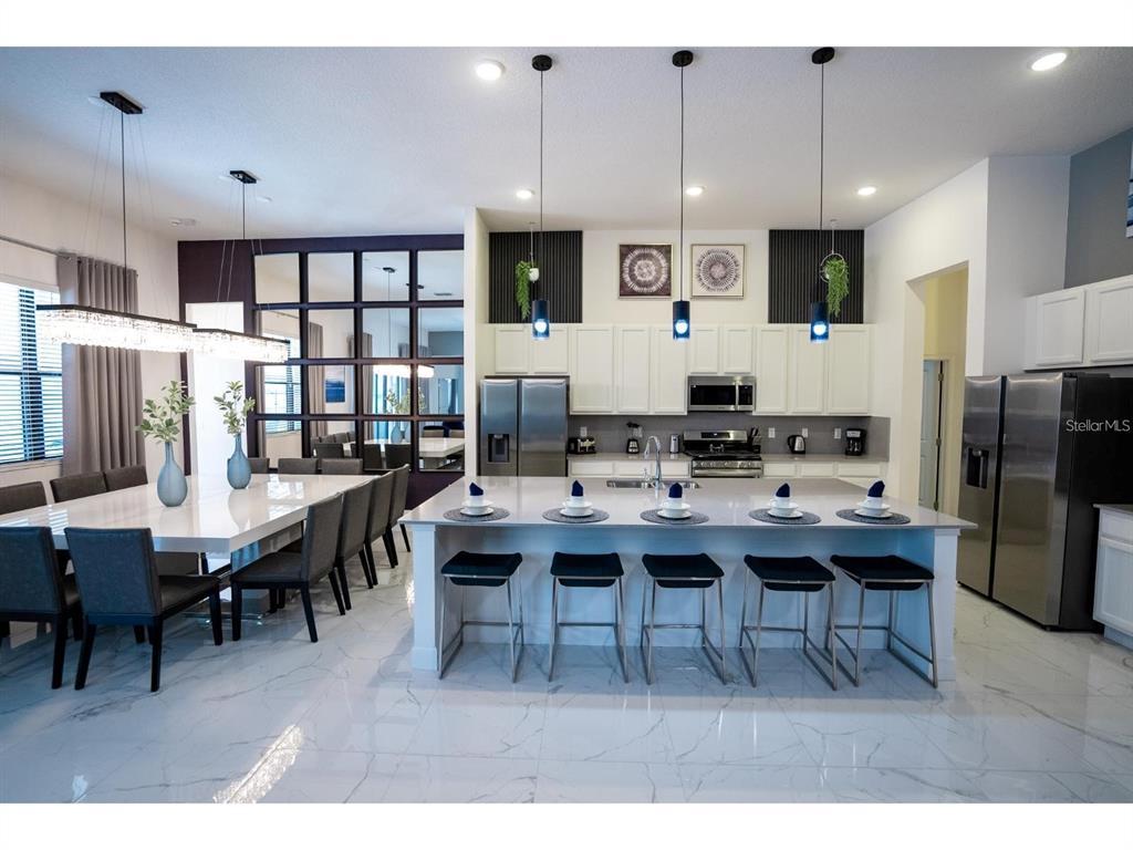 A modern kitchen and dining area features white cabinetry, a large island, and marble flooring — 1443 BUTTERFLY MILKWEED COURT, DAVENPORT, FL