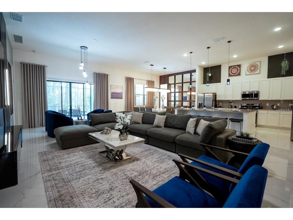 A spacious open-concept living room features a large sectional sofa, blue armchairs, and a kitchen — 1443 BUTTERFLY MILKWEED COURT, DAVENPORT, FL
