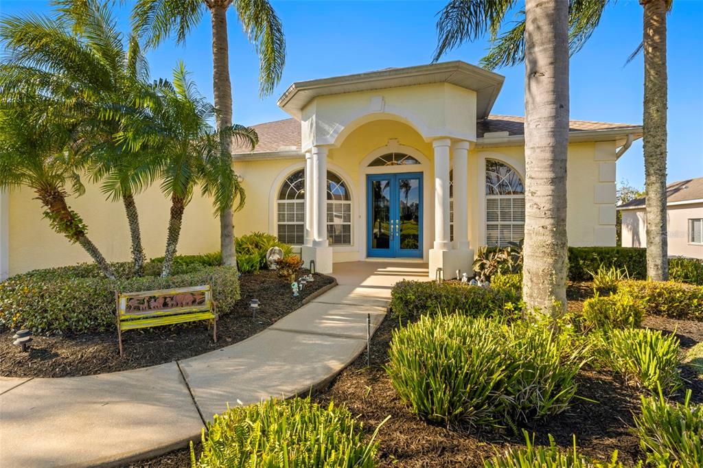 A yellow house exterior features a front walkway, palm trees, and a blue double door — 13235 LEGENDS TRAIL, DADE CITY, FL