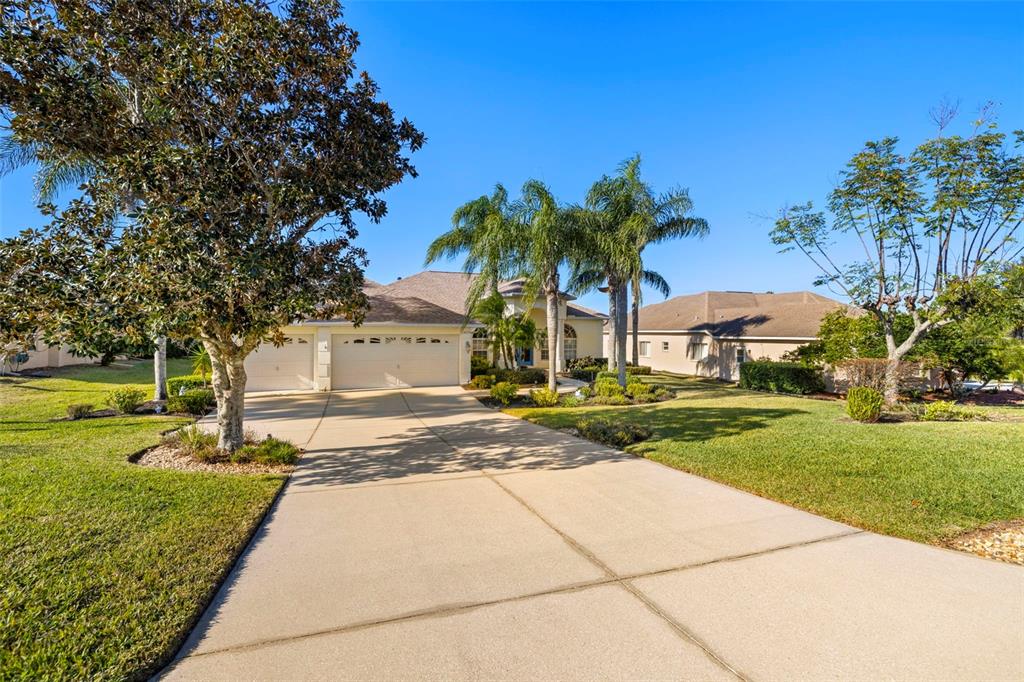 A beige house with a three-car garage and palm trees sits at the end of a driveway — 13235 LEGENDS TRAIL, DADE CITY, FL