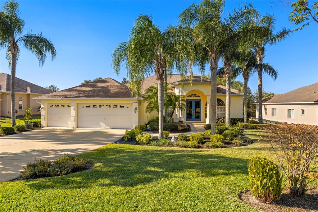 A single-story yellow house with a three-car garage and palm trees in the front yard — 13235 LEGENDS TRAIL, DADE CITY, FL
