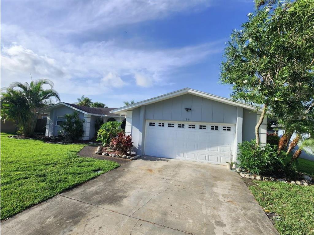 A single-story house with a white garage door, light blue siding, and a concrete driveway — 128 98TH AVENUE N, ST PETERSBURG, FL