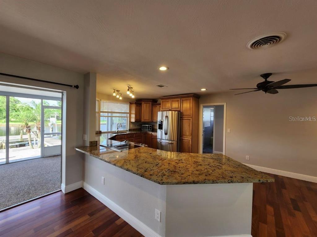 A kitchen with granite countertops, wooden cabinets, and stainless steel appliances overlooks a screened patio — 128 98TH AVENUE N, ST PETERSBURG, FL