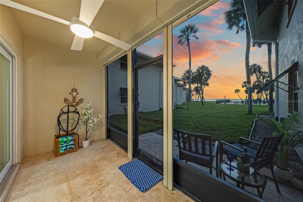 A screened-in patio with tile flooring overlooks a grassy lawn and palm trees at sunset — 4660 OCEAN BOULEVARD UNIT F1, SARASOTA, FL