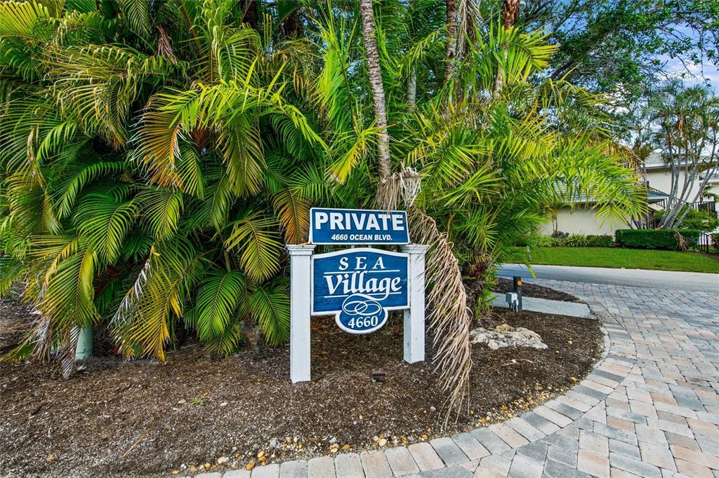 A blue and white sign for Sea Village stands in front of lush palm trees — 4660 OCEAN BOULEVARD UNIT F1, SARASOTA, FL