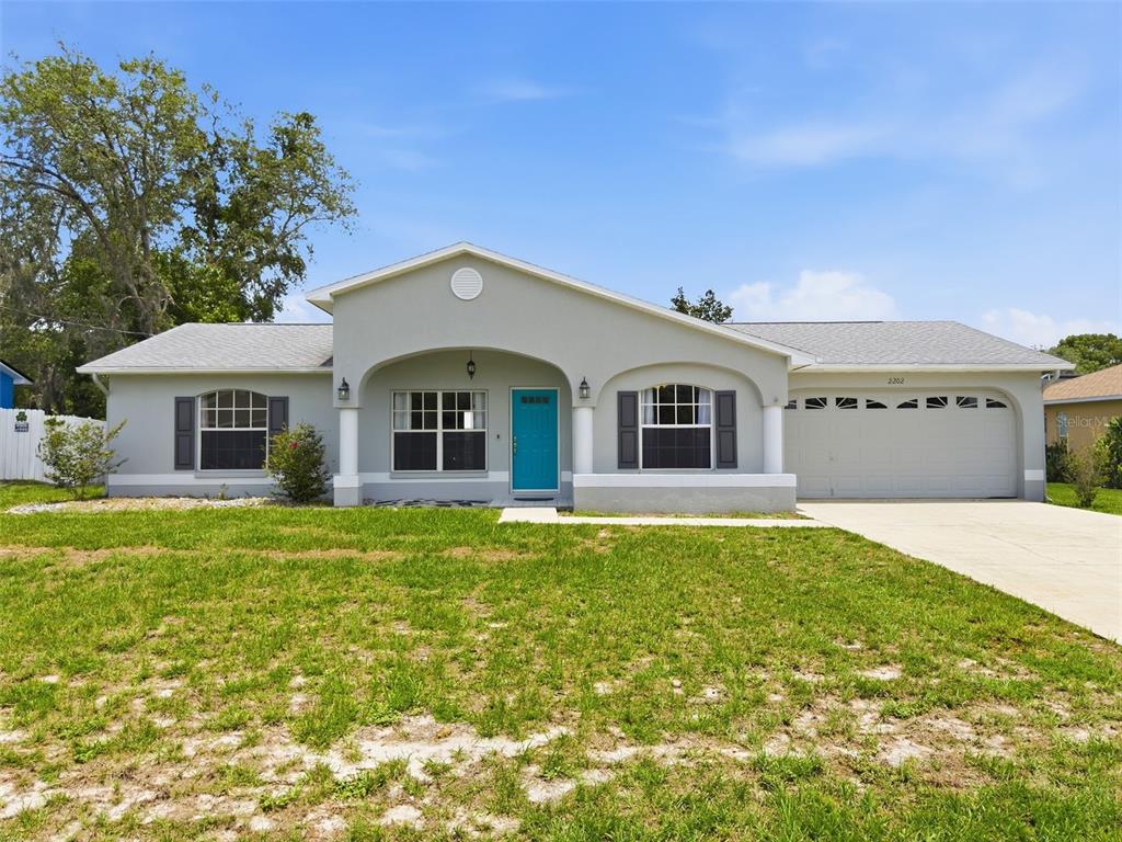 A single-story house with a light gray exterior, a teal front door, and a two-car garage — 2202 GODFREY AVENUE, SPRING HILL, FL