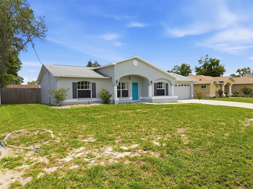 A single-story house with a light gray exterior, a bright blue front door, and a lawn — 2202 GODFREY AVENUE, SPRING HILL, FL