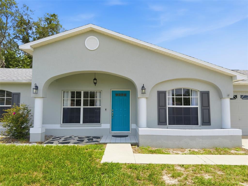 A light gray house features a bright blue front door, arched porch, and white columns — 2202 GODFREY AVENUE, SPRING HILL, FL