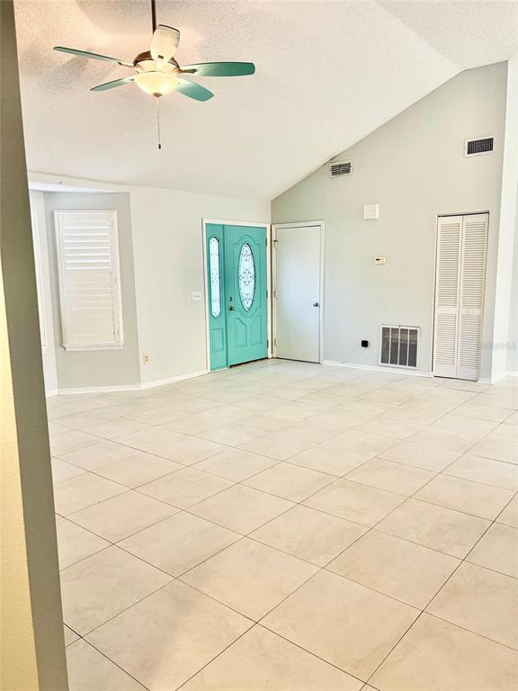 A bright living room features light-colored tile floors, a vaulted ceiling, and a teal front door — 2720 BANYAN DRIVE, EDGEWATER, FL