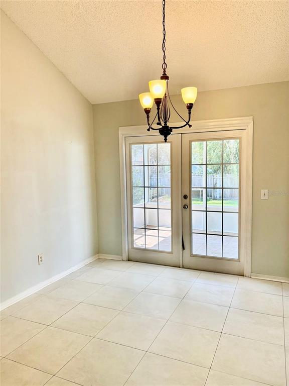 A dining area features light-colored floor tiles, a chandelier, and glass French doors leading outside — 2720 BANYAN DRIVE, EDGEWATER, FL