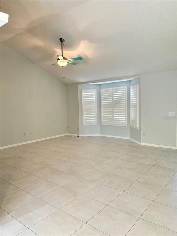 An empty living room features light-colored tile flooring, a vaulted ceiling with a fan, and bay windows — 2720 BANYAN DRIVE, EDGEWATER, FL