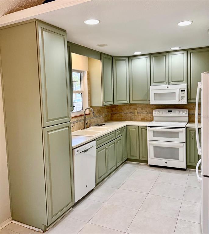 A kitchen features sage green cabinets, white appliances, a tiled backsplash, and light-colored floor tiles — 2720 BANYAN DRIVE, EDGEWATER, FL