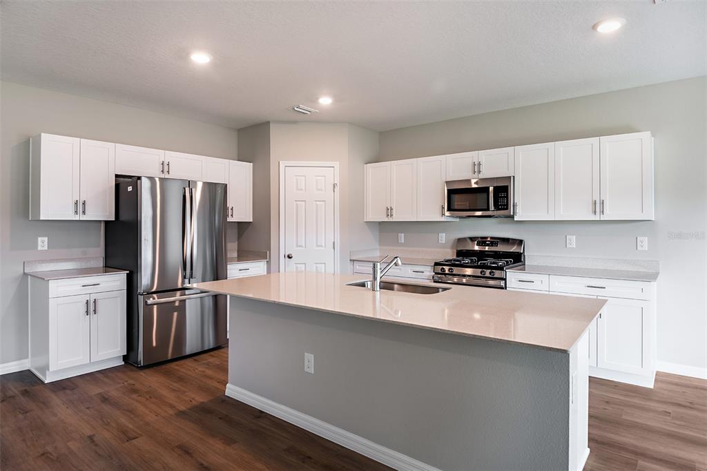 A modern kitchen features white cabinets, stainless steel appliances, and a large central island — 33647 NOBLE CREEK PLACE, DADE CITY, FL