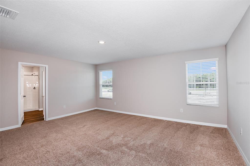 An empty bedroom with beige carpet, light gray walls, two windows, and an attached bathroom — 33647 NOBLE CREEK PLACE, DADE CITY, FL