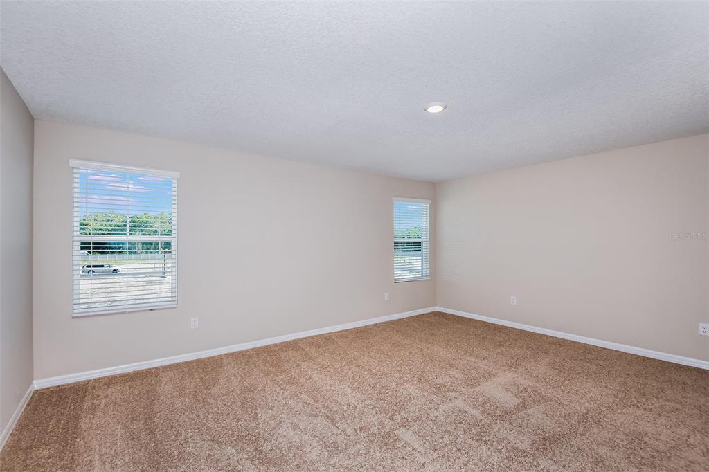 An empty bedroom features beige walls, tan carpeting, two windows with blinds, and recessed lighting — 33647 NOBLE CREEK PLACE, DADE CITY, FL