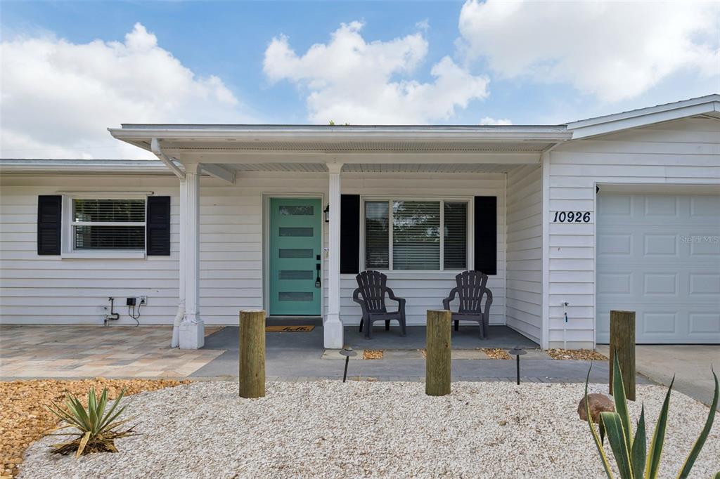 The exterior of a white house features a teal front door and a covered porch — 10926 TEMPLE AVENUE, SEMINOLE, FL