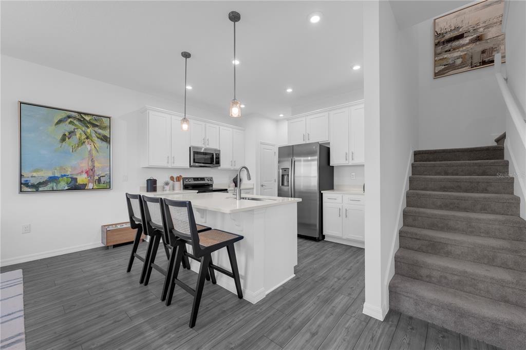 A modern kitchen features white cabinets, a central island with bar seating, and gray flooring — 10079 MORNING MEADOWLARK TRAIL, PARRISH, FL
