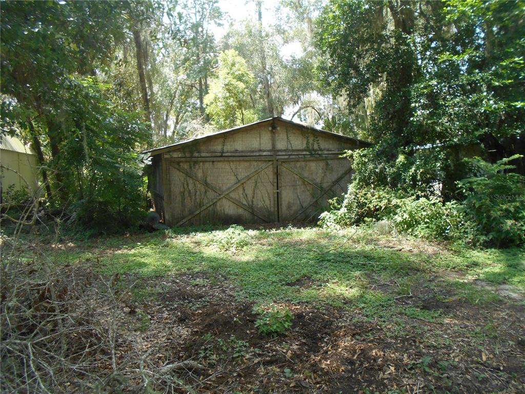 A weathered wooden shed with double doors stands in a wooded, overgrown yard — 18800 NE 248TH TERRACE, FORT MC COY, FL