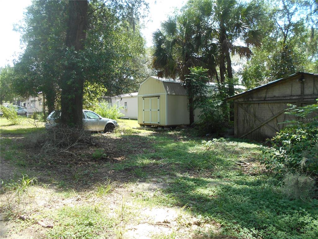 A yard features a light-colored storage shed, a wooden structure, and a parked silver car — 18800 NE 248TH TERRACE, FORT MC COY, FL