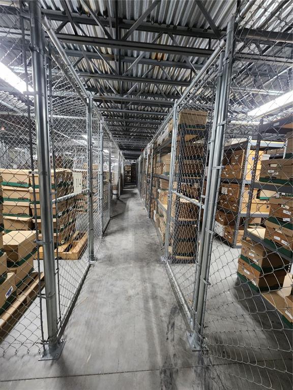 A narrow warehouse aisle features metal shelving units enclosed by chain-link fencing — 711 N 3RD ST, LEESBURG, FL