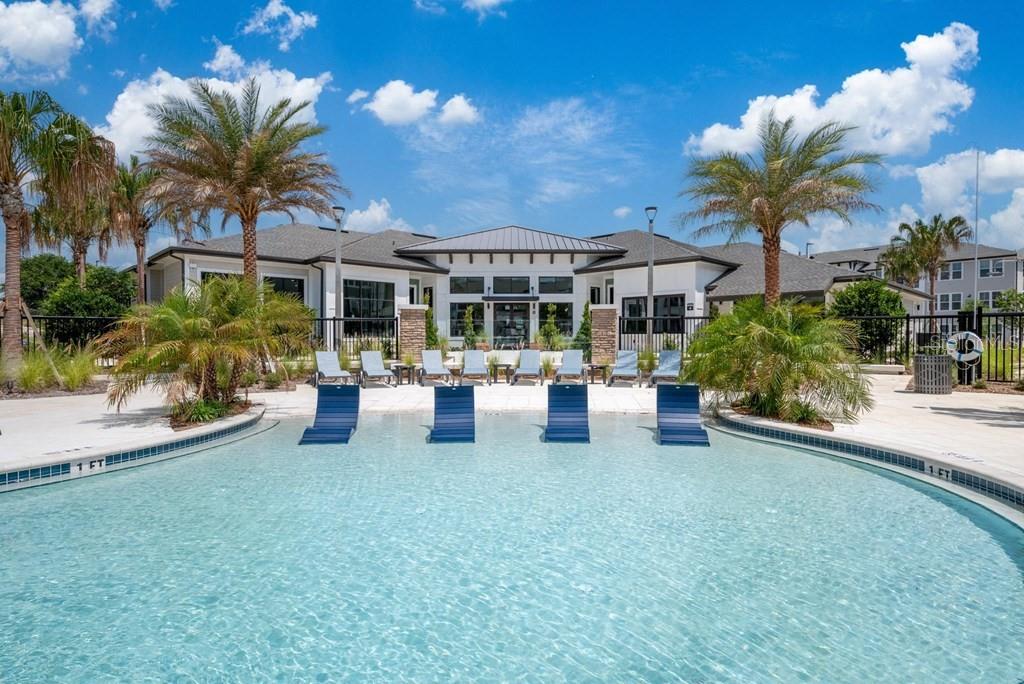 A swimming pool with lounge chairs sits in front of a modern clubhouse building — 15000 STRATUS LOOP UNIT C1, WINTER GARDEN, FL