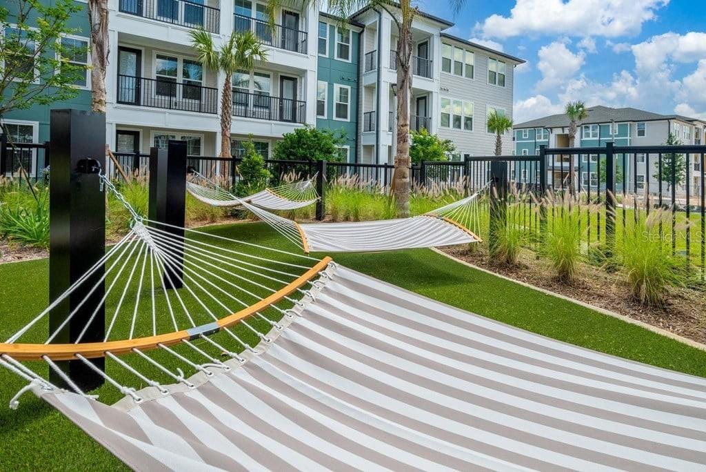 Three striped hammocks are suspended on a grassy lawn in front of a modern apartment building — 15000 STRATUS LOOP UNIT C1, WINTER GARDEN, FL