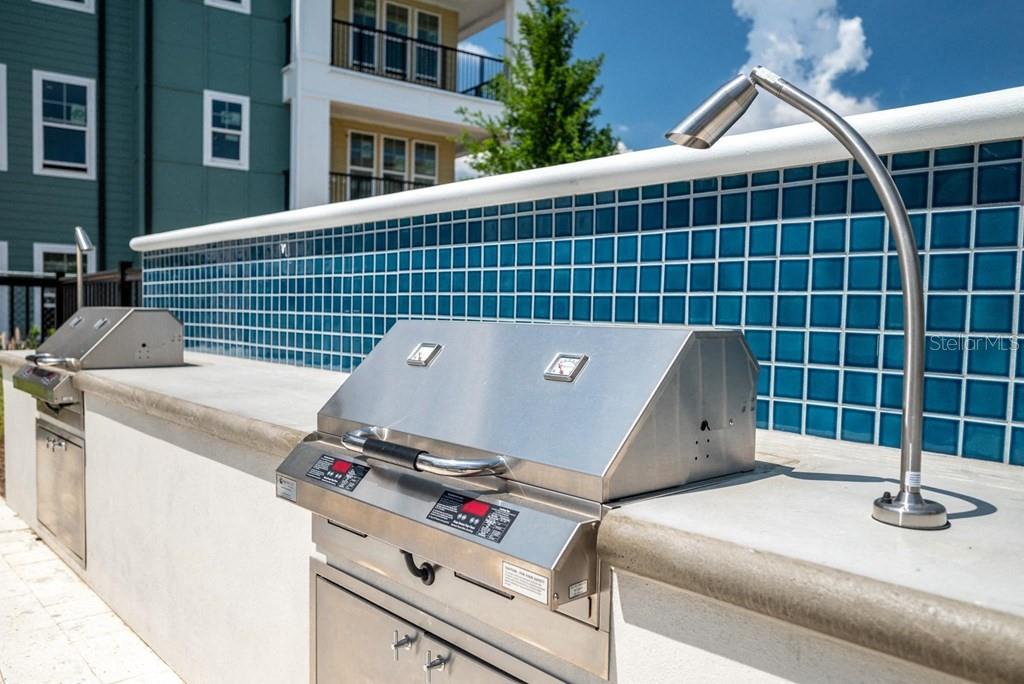 An outdoor kitchen area features stainless steel grills set into a concrete counter with blue tiles — 15000 STRATUS LOOP UNIT C1, WINTER GARDEN, FL
