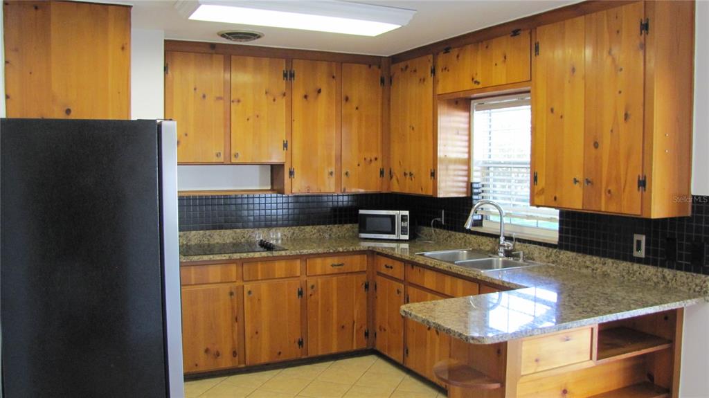 A kitchen with knotty pine cabinets, granite countertops, and a black tiled backsplash — 1803 W LOUISIANA AVENUE, TAMPA, FL