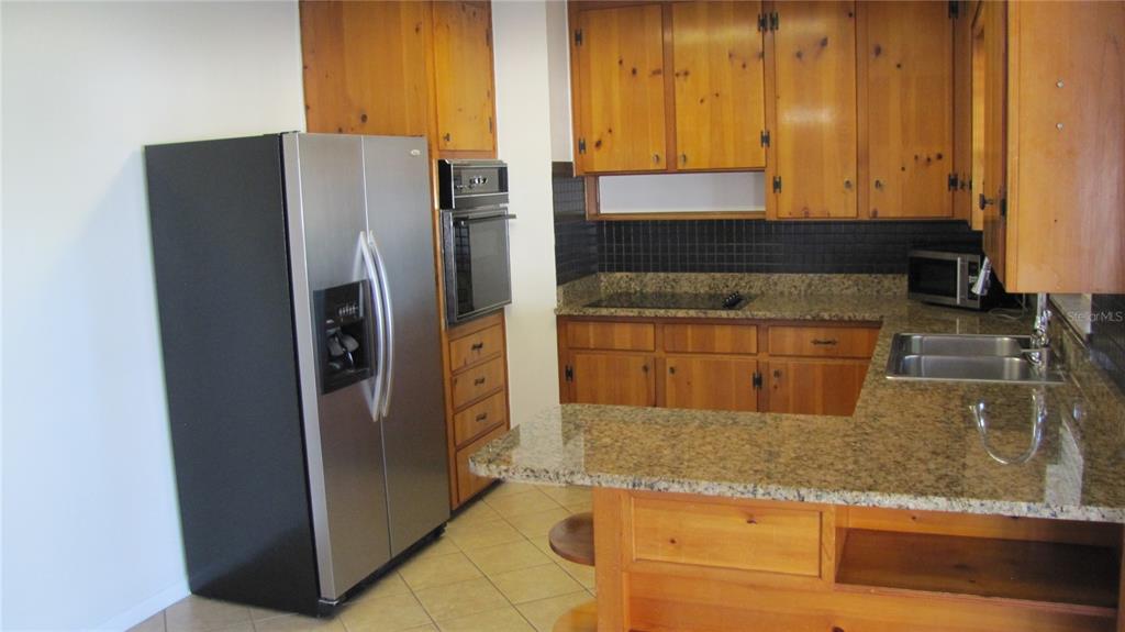 A kitchen features wood cabinets, granite countertops, a stainless steel refrigerator, and a wall oven — 1803 W LOUISIANA AVENUE, TAMPA, FL