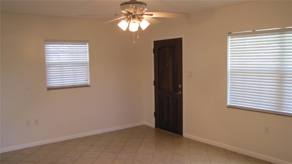 A room with beige tile floors, white walls, a ceiling fan, and a dark wood door — 1803 W LOUISIANA AVENUE, TAMPA, FL
