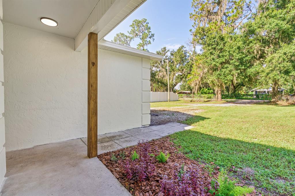 A concrete patio with a wooden support post overlooks a grassy yard and wooded area — 414 S WIGGINS ROAD, PLANT CITY, FL