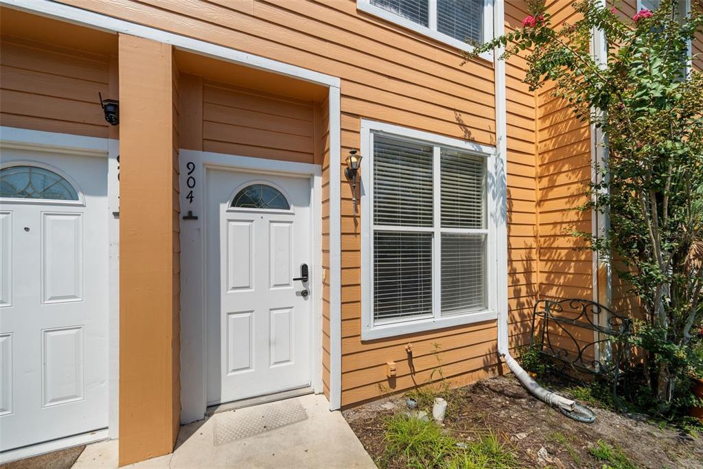 The exterior of a tan-sided townhouse features a white front door with the number 904 — 3970 SW 20TH AVENUE UNIT 904, GAINESVILLE, FL