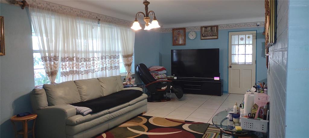 A living room features light blue walls, a light-colored sofa, a large television, and tile flooring — 6165 26TH AVENUE N, ST PETERSBURG, FL