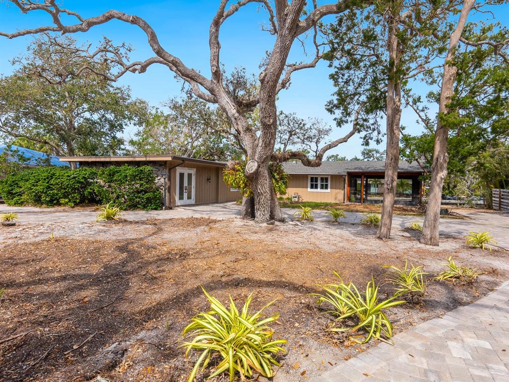 A single-story house with wood siding and a stone wall sits behind a large tree — 615 BUTTONWOOD DRIVE, LONGBOAT KEY, FL