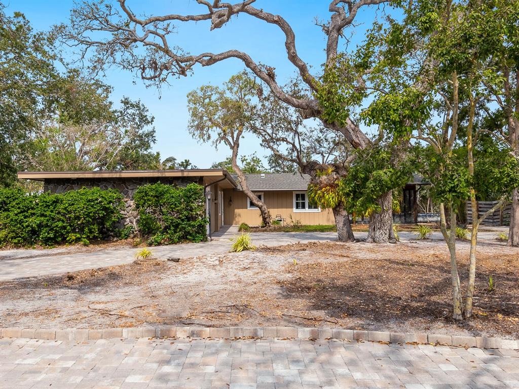 A single-story house with stone siding and wood paneling sits behind large oak trees — 615 BUTTONWOOD DRIVE, LONGBOAT KEY, FL