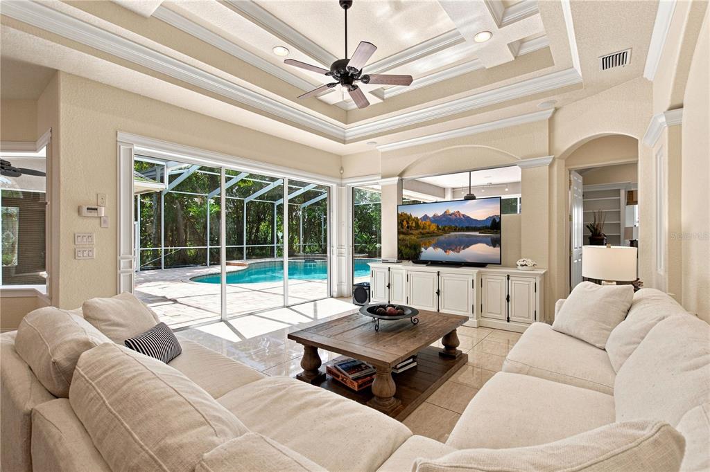 A living room with a tray ceiling, white sofa, coffee table, and sliding doors to a pool — 9469 WATERFORD OAKS DRIVE, WINTER HAVEN, FL