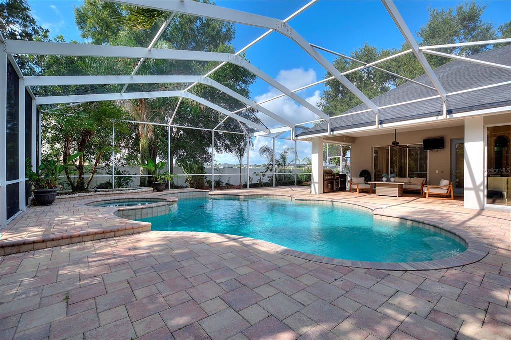 A screened-in patio features a swimming pool, a hot tub, and a paved deck — 9469 WATERFORD OAKS DRIVE, WINTER HAVEN, FL