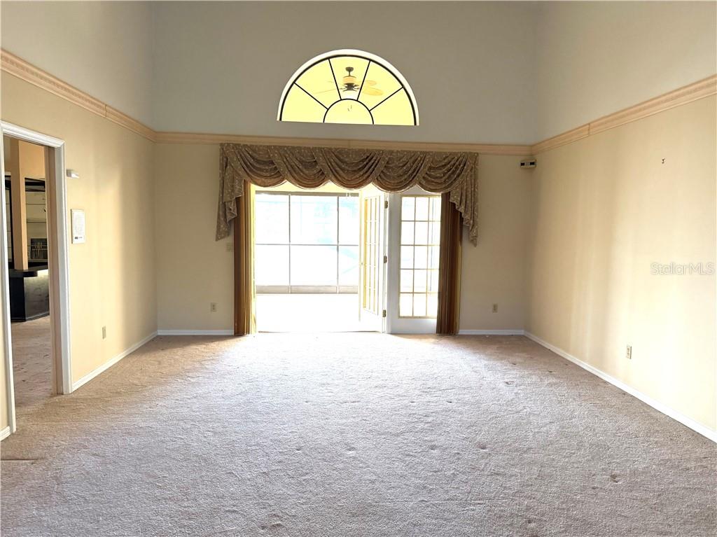 A carpeted living room features a vaulted ceiling, an arched window, and glass patio doors — 6135 W Pine Ridge BOULEVARD, BEVERLY HILLS, FL