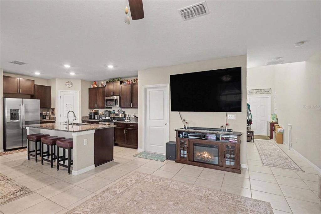 An open-concept kitchen with dark cabinets and an island overlooks a living area with a fireplace — 3166 OYSTER COVE STREET, WIMAUMA, FL