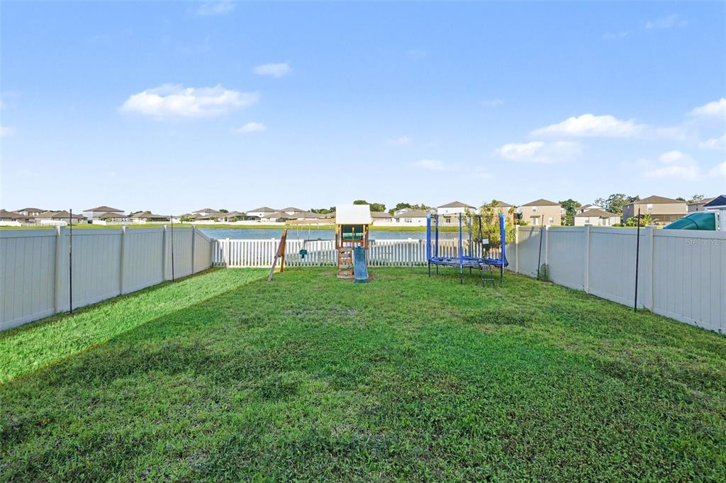 A fenced backyard features a grassy lawn, a wooden playset, and a blue trampoline — 3166 OYSTER COVE STREET, WIMAUMA, FL