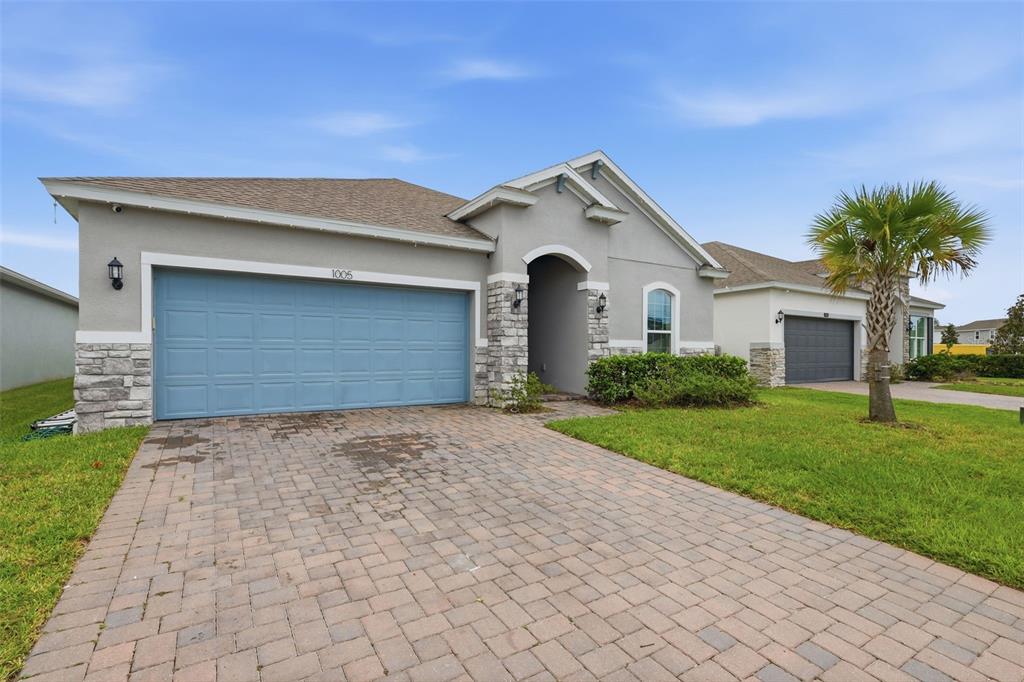 A single-story house with a blue garage door, stone accents, and a paved driveway — 1005 CHELAN FALLS DRIVE, DELAND, FL