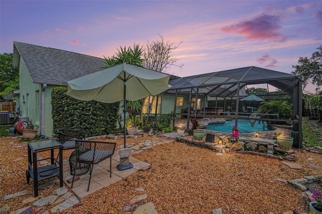 A backyard features a gravel patio, a patio umbrella, metal chairs, and a screened-in pool — 927 JAMESTOWN DRIVE, ROCKLEDGE, FL