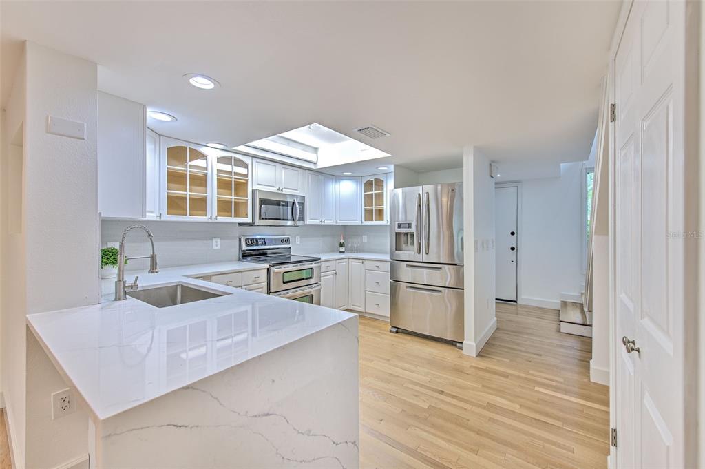 A modern kitchen features white cabinetry, stainless steel appliances, a marble-topped island, and hardwood floors — 1028 APOLLO BEACH BOULEVARD UNIT 4, APOLLO BEACH, FL
