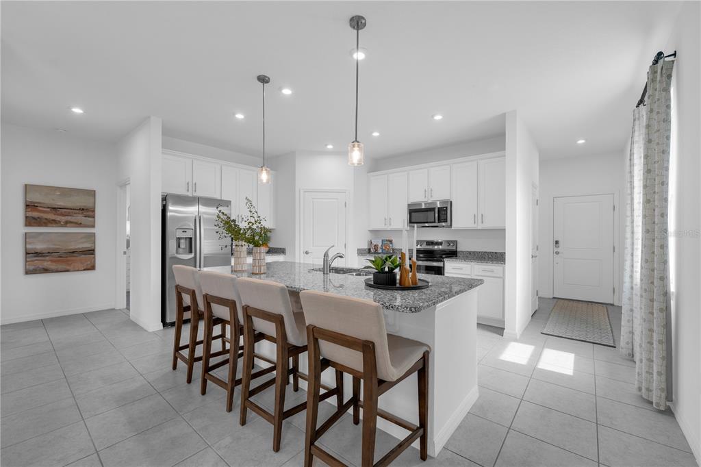 A modern kitchen features white cabinets, granite countertops, a central island with barstools, and tile flooring — 10123 MORNING MEADOWLARK TRAIL, PARRISH, FL